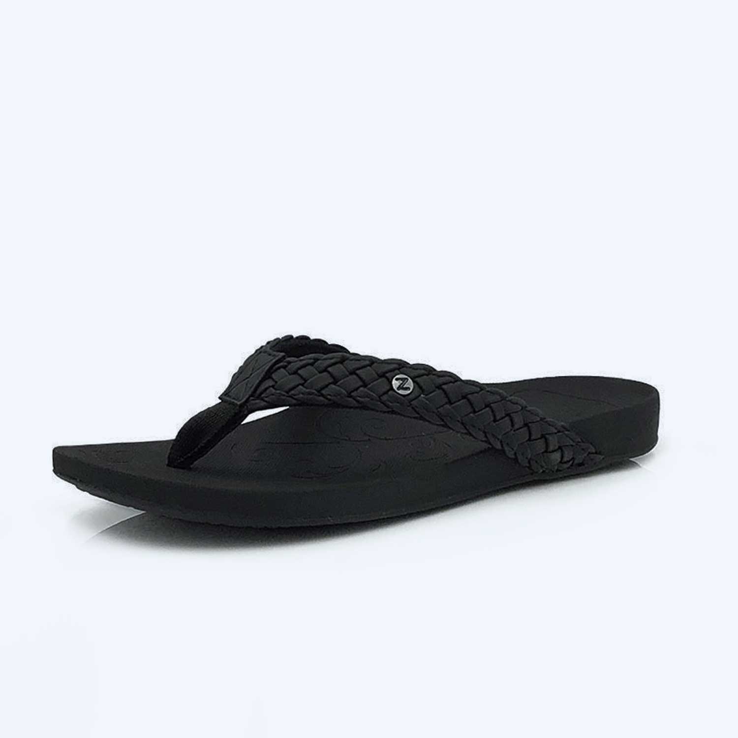 The Tiki Girl – Indigo is a black flip-flop sandal featuring a braided strap and a small round metal accent on the side, displayed against a plain light background.