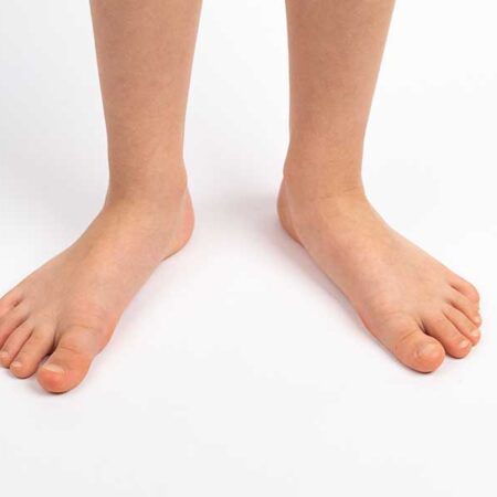 Bare feet of a person standing on a white surface, with legs visible from the knees down.