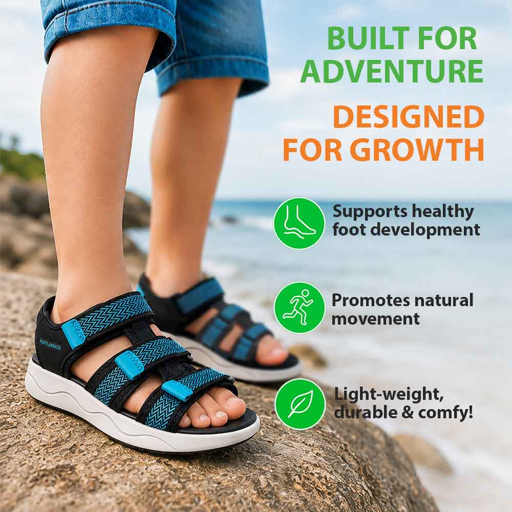 A child stands on a rocky beach wearing 'Arch-Up' sandals in Black/Blue, showcasing their support, comfort, and design that encourages natural foot movement.