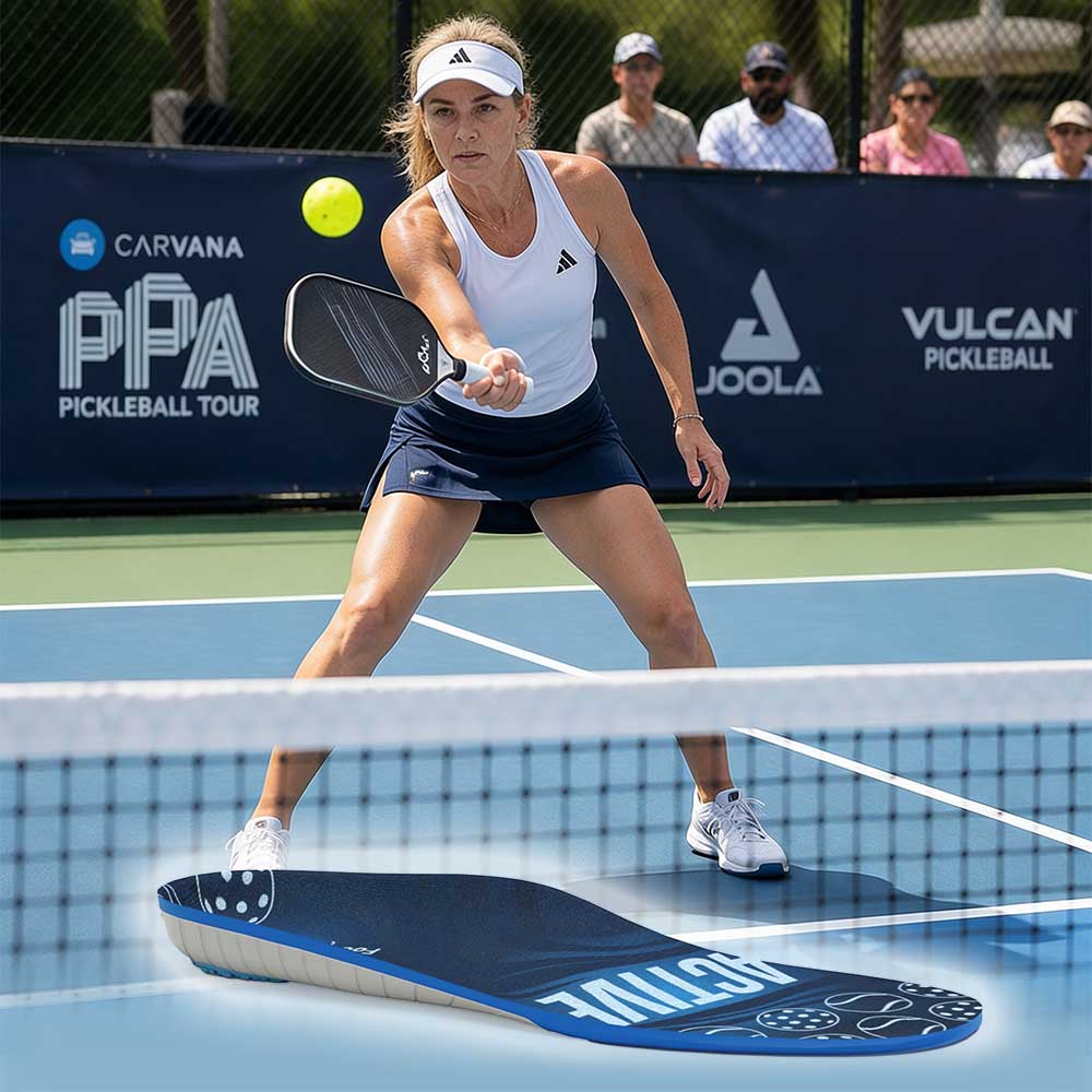 A woman playing pickleball on an outdoor court prepares to hit a ball with her paddle; banners and a net are visible in the background.